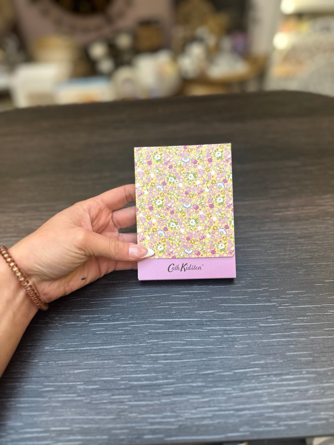 Carnet fermé à couverture fleurie jaune et rose portant le logo Cath Kidston